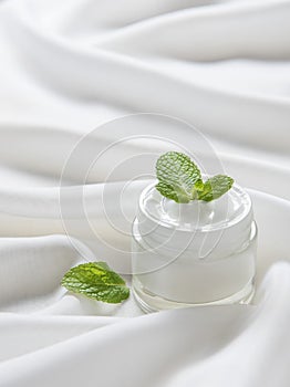 The moisturizing cream with green young leaves on the white silk