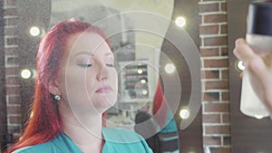 Moisturizing spray sprinkles on the face of the woman after makeup procedure