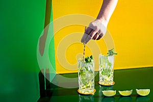 Mojito alcoholic cocktail with barman hand stirring ice on colorful background . New modern cocktails drinks design concept