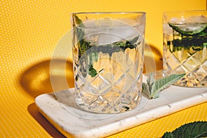 Mojito alcoholic cocktails with alcohol, rum lime, mint and ice with hard lights on yellow background. Mixology details and close photo