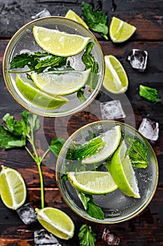 Mojito cocktail drink with lime, Ice and mint. Black wooden background. Top view