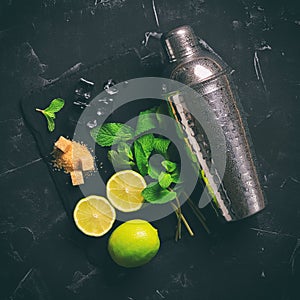 Mojito cocktail ingredients. Mint leaves, lime, ice cubes, brown sugar, and a shaker. Black stone background. Toned. Top view,