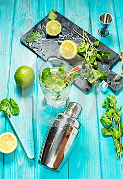 Mojito cocktail with lime and mint in highball glass on a blue wood table. Drink making tools and ingredients for cocktail