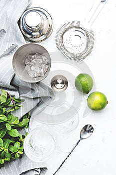 Mojito cocktail making. Mint, lime, ice - ingredients and steel bar tools. Top view, white table background, copy space