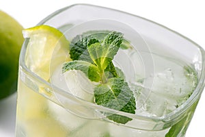 Mojito glass with mint leaves, sliced lime and ice close-up on white background