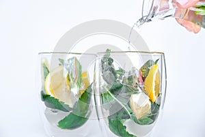 Mojito refreshing cocktail pouring, alcohol drink. Lemonade with lemon and mint leaves on light background. Ice cubes