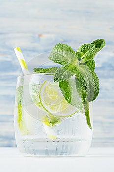 Mojito in wet glass with mint, slices lime, ice cubes, straw on soft blue background, closeup.