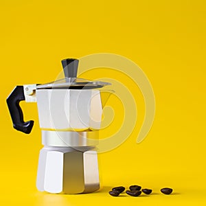 Moka coffee pot and beans roast on yellow paper background. Copy space for text