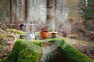 Moka pot coffee maker and wooden cup kuksa on a beautiful moss covered stump. The background of the forest is blurred