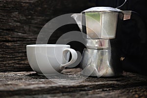 Moka pot and white coffee cup on rustic wooden background