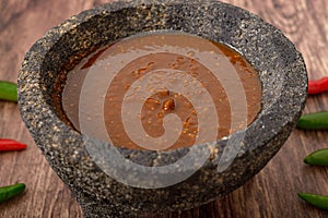 Molcajete with hot sauce on wooden table with chili peppers around