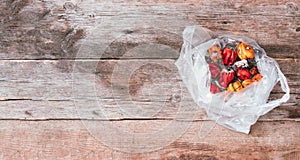 Moldy and wrinkled rotten peppers in plastic bag on wooden background. Concept of unhealthy, decompose, spoiled vegetables.