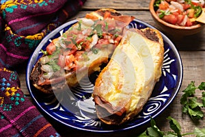 Molletes with ham, refried beans and melted cheese on a wooden background. Mexican food photo