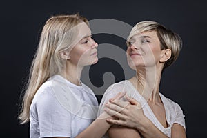 Mom and adult daughter hug and smile. Beautiful blondes in light T-shirts look at each other. Love and tenderness. Close-up. Black