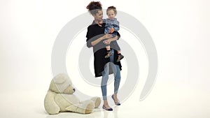 Mom african american keeps the baby and on the floor a toy bear. White background. Slow motion