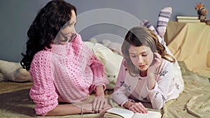 Mom attentively listening her daughter reading bedtime storybook, happy family