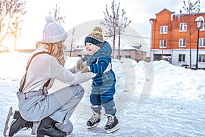Mom with baby boy 3-5 years old, learn to train, ride in winter city on rink, ice skating. Happy smiling children play