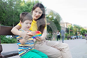 Mom and baby boy 4 years old play with a colored trendy toy Pop it in the park in nature. Antistress sensitive toy or