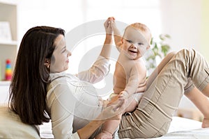 Mom and baby boy in diaper playing in sunny room. Mother and little kid relaxing at home. Family having fun together.