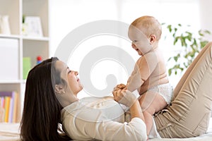 Mom and baby boy in diaper playing in sunny room. Mother and little kid relaxing at home. Family having fun together.