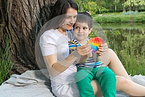 Mom and baby boy 4 years old play with a colored trendy toy Pop it in the park in nature. Antistress sensitive toy or photo