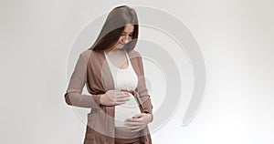 Mom and baby connection. Young pregnant woman caressing her belly with love and tender, white studio background