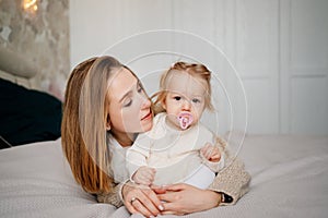 mom and baby daughter with baby nipple play and hug in bed. games with children.