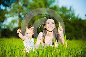 Mom and baby girl laying on grass and cheerfully catching soap b