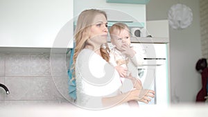 Mom with baby going in white kitchen. Beauty woman with little child on hand