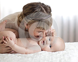 Mom and baby playing in sunny bedroom. Mother and little child relaxing at home. Family having fun together.