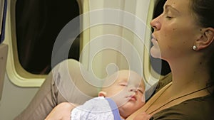 Mom and baby are resting on the plane during the flight. Night flight over the ocean. The child's eyes are closed