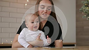 Mom and and baby sitting at the table playing tablet computer pressing your fingers on the screen and laughing