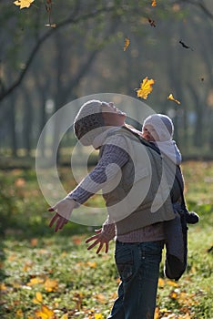 Mom and baby in a sling rejoice falling autumn leaves