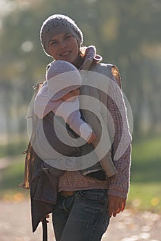 Mom and baby in a sling rejoice falling autumn leaves