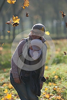 Mom and baby in a sling rejoice falling autumn leaves