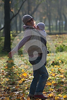 Mom and baby in a sling rejoice falling autumn leaves