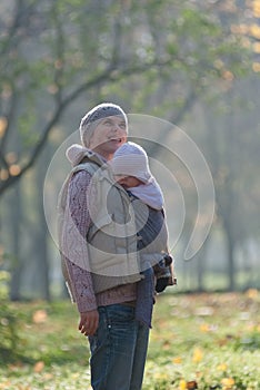 Mom and baby in a sling rejoice falling autumn leaves