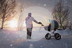 Mom with a baby in a stroller in winter at sunset on a frosty day