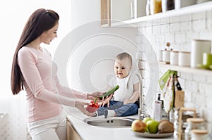 Mom with baby washing vegetables at kitchen, empty space