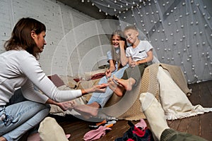 Mom in the bedroom on the bed fun tickles the legs of children, boys and girls.