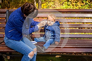 Mom on a bench in the park wipes the baby face with a napkin, which got dirty while playing for a walk. close-up, soft