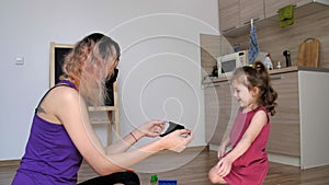 Mom in a black protective medical mask is trying to put a mask on her daughter.