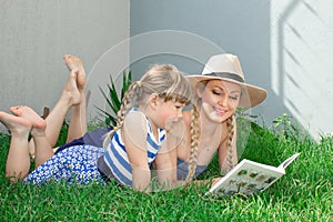 Mom blonde and daughter are lying on the grass and reading a book, happy family. photo