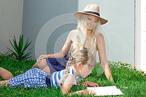 Mom blonde and daughter are lying on the grass and reading a book, happy family. photo