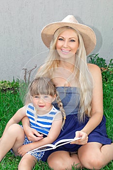 Mom blonde and daughter are lying on the grass and reading a book, happy family. photo