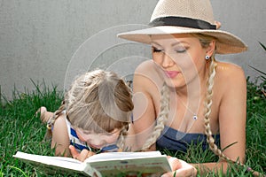 Mom blonde and daughter are lying on the grass and reading a book, happy family. photo