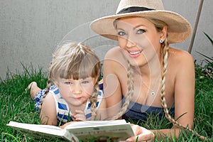 Mom blonde and daughter are lying on the grass and reading a book, happy family. photo