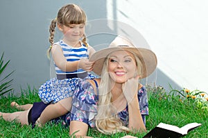 Mom blonde in a hat and her daughter are lying on the grass and reading a book, happy family. photo