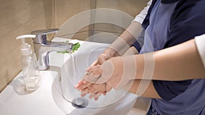 Mom and boy washing hands together. Mother helps her son directing arms under running water. Parenthood concept. Side