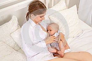 Mom breastfeed baby 6 months old lying on a white bed, baby feeding, place for text